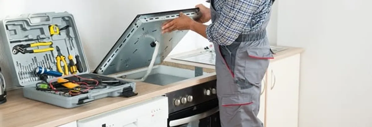 Cooktop repair technician lifting a built-in stovetop for service in St Paul, MN