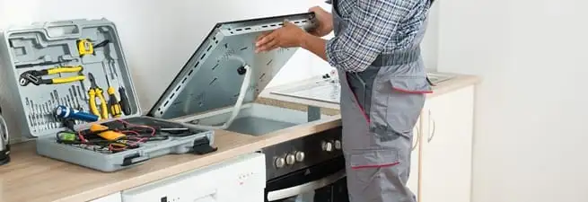 Cooktop repair technician lifting a built-in stovetop for service in St Paul, MN