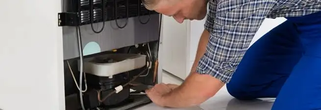 Refrigerator repair technician servicing the compressor and condenser area in St Paul, MN