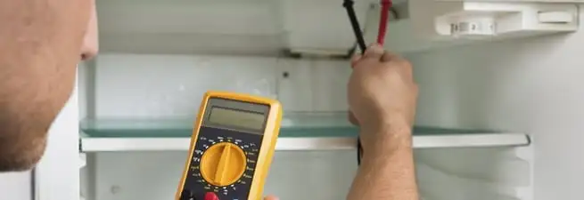 Refrigerator repair technician testing electrical components with a multimeter in St Paul, MN